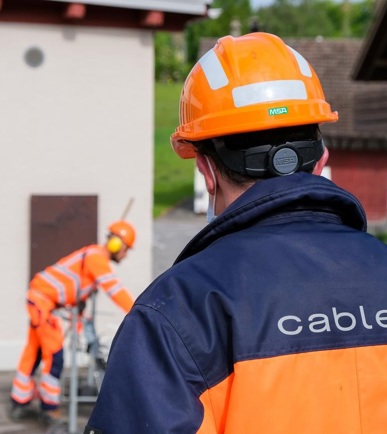 Ein cablex-Mitarbeiter von hinten mit cablex-Jacke und orangem Helm